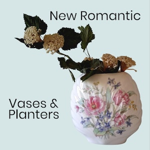 May include: A white, round vase with a floral design featuring pink and blue flowers. The vase is filled with dried flowers and greenery. The text "New Romantic" and "Vases & Planters" are displayed.