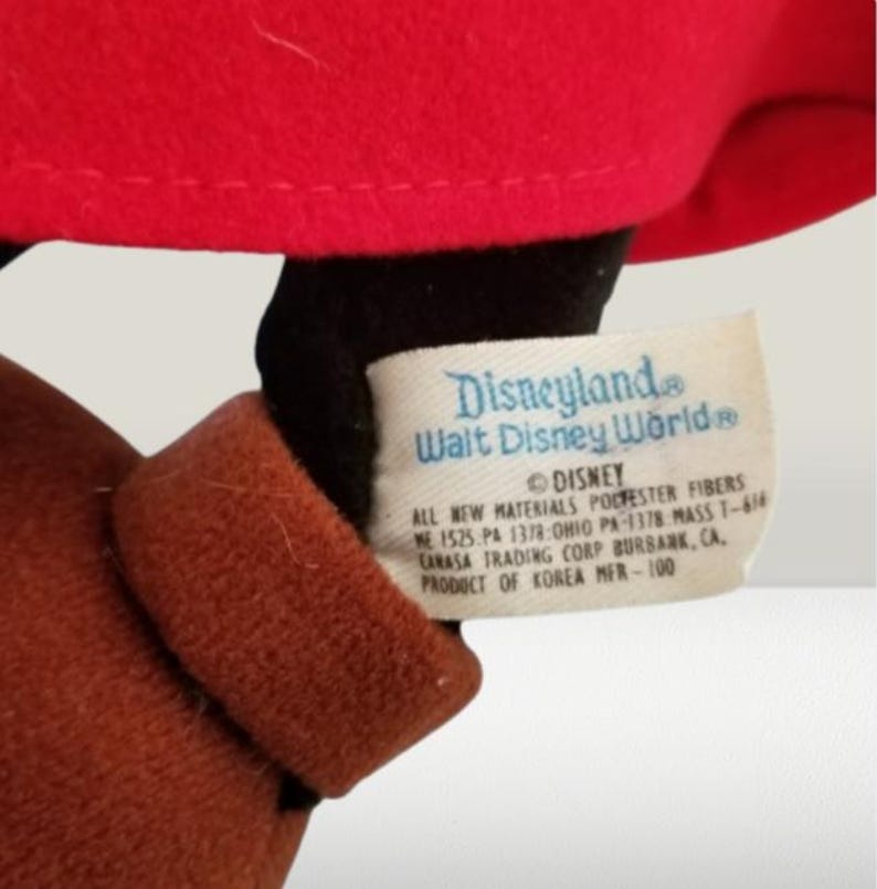 May include: A brown and black plush Mickey Mouse toy wearing a red hat with a white tag that reads "Disneyland Walt Disney World&reg; DISNEY ALL NEW MATERIALS POLYESTER FIBERS WE 1525. PA 1378:OHIO PA-1378 MASS T-618 CARASA TRADING CORP BURBANK, CA. PRODUCT OF KOREA MER-100"