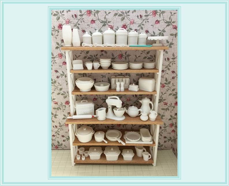 May include: A white kitchen shelving unit with four shelves filled with white dishes, bowls, canisters, and kitchen tools. The shelving unit is against a floral wallpaper background.