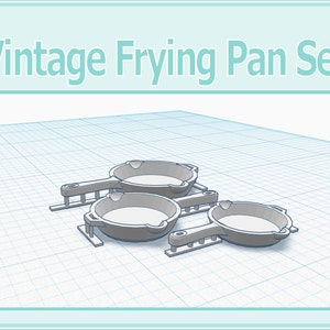 Op de afbeelding: Een set van drie vintage-stijl braadpannen met handvatten. De pannen zijn zilverkleurig en hebben een licht verweerde uitstraling. Ze zijn gestapeld op een witte rasterachtergrond.