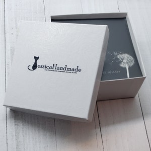 K&ouml;nnte beinhalten: Wei&szlig;e Geschenkbox mit einem schwarzen Katzenlogo, auf dem "JessicaHandmade Your Personalised Handmade Jewellery & Gifts" steht. Die Box ist ge&ouml;ffnet und zeigt eine graue Karte mit einem wei&szlig;en L&ouml;wenzahn und dem Text "Beste W&uuml;nsche".