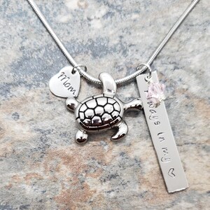 K&ouml;nnte beinhalten: Silberne Halskette mit einem Schildkr&ouml;ten-Anh&auml;nger, einem Herz-Anh&auml;nger mit der Gravur "Mom" und einem Barren-Anh&auml;nger mit der Gravur "Always in my heart".