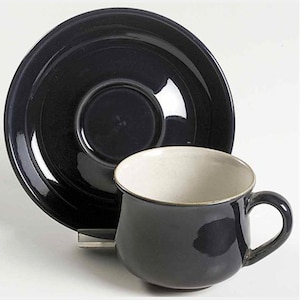 Könnte beinhalten: Ein dunkelblaues Porzellan-Teetassen-Set. Die Tasse hat ein weißes Inneres und eine abgerundete Form. Die Untertasse hat einen leicht erhöhten Rand.