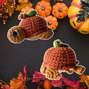 Può includere: Due giocattoli di tartaruga a forma di zucca all'uncinetto. Le tartarughe sono marroni e arancioni con una superficie all'uncinetto testurizzata.