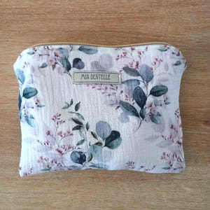 May include: A white floral print pouch with a gold zipper. The pouch features a pattern of green and blue leaves and small pink flowers. The text "MIA DENTELLE" is printed on a small rectangular label.