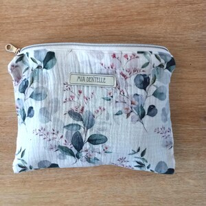 May include: A rectangular, floral-patterned pouch with a zipper closure. The pouch features a white background with a delicate print of green and purple leaves and flowers. The text "MIA DENTELLE" is printed on a small label.