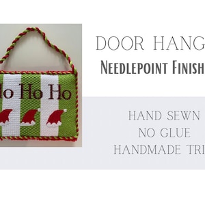 May include: A rectangular Christmas door hanger with green and white stripes, embroidered with "Ho Ho Ho" and Santa hats. The trim is red and green, with a matching braided handle. The text on the image says "Door Hanger, Needlepoint Finishing, Hand Sewn, No Glue, Handmade Trim."
