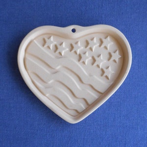 May include: A white heart-shaped cookie cutter with a design of the American flag, featuring red and white stripes and blue stars.