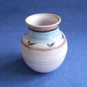 May include: A small white ceramic vase with a blue and red design. The vase has a rounded body and a narrow opening.