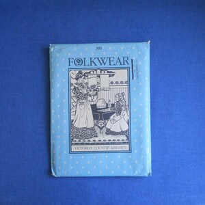 Può includere: Una busta di cartamodello per cucito blu e bianca con il testo "Folkwear" e "Victoria's Country Kitchen" stampato su di essa. La busta presenta un'illustrazione in bianco e nero di due donne in un ambiente da cucina.