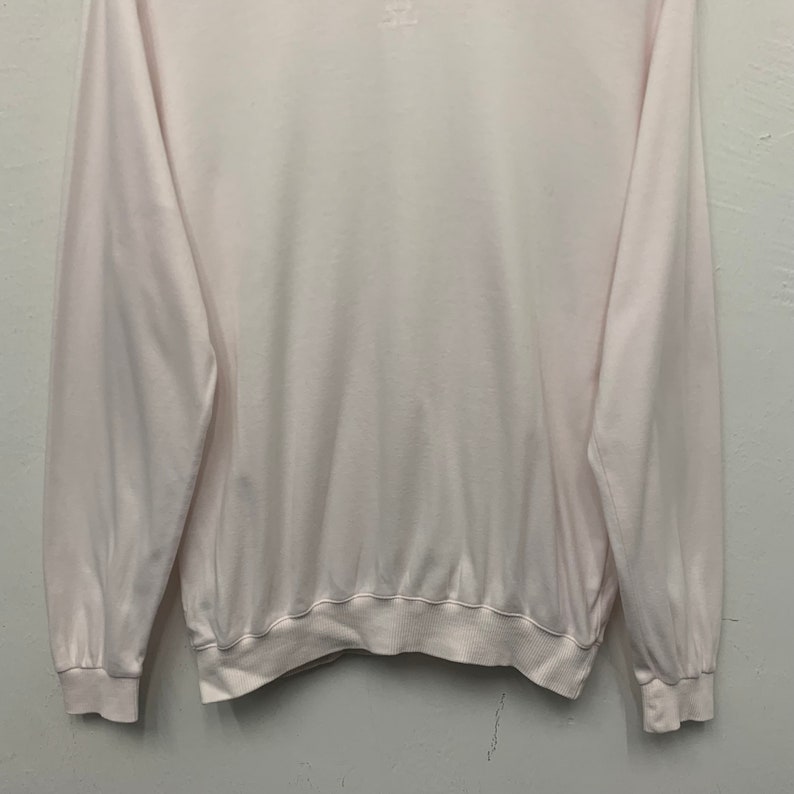 May include: A pale pink long-sleeved sweatshirt with a ribbed hem and cuffs. The crew neck sweatshirt has a small logo on the upper back. The fabric appears soft and lightweight, suitable for casual wear.
