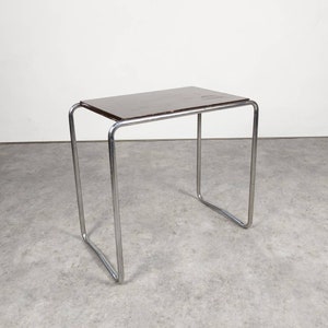 Può includere: Tavolino rettangolare con piano marrone scuro e struttura tubolare in acciaio cromato. Il tavolo misura circa 51 cm di lunghezza, 30 cm di larghezza e 46 cm di altezza. Design minimalista e moderno.