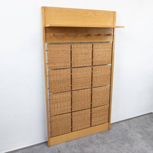 Könnte beinhalten: Ein Wand-Kleiderständer aus Holz mit einer geflochtenen Weidenholz-Verkleidung und einem Regal. Der Kleiderständer hat mehrere Haken zum Aufhängen von Mänteln, Hüten oder Taschen.