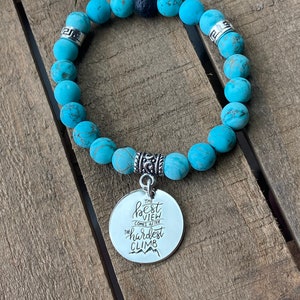Op de afbeelding: Turquoise kralen armband met een zilveren bedel met de tekst "Het beste uitzicht komt na de moeilijkste klim".