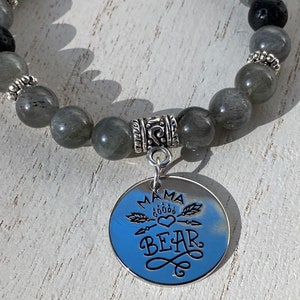 May include: Gray gemstone bracelet with a silver charm that says "Mama Bear" with a heart and paw print design.