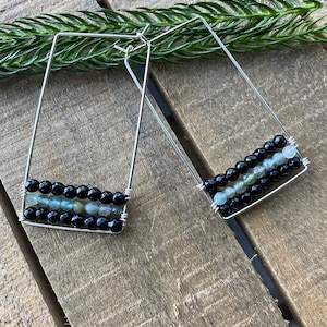 May include: A pair of silver hoop earrings with black and green gemstone beads. The earrings are rectangular in shape and have a modern design.