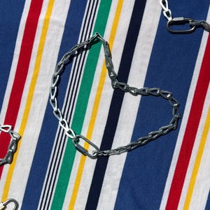 May include: A silver chain necklace with a carabiner clasp. The necklace is laying on a striped fabric background.