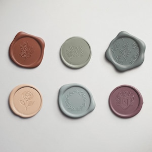 May include: An overhead shot of six wax seals in various colors, including terracotta, sage green, and dusty rose. Each seal features a different embossed design, such as a floral sprig, a rose, and a laurel wreath. One seal has the text "WAX SEALS STUDIO".
