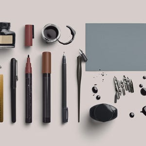 May include: An assortment of calligraphy and drawing supplies, including ink bottles, pens, markers, nibs, and a ruler. The items are arranged on a light background, with ink splatters adding a creative touch. The color palette is primarily black, brown, and gold.