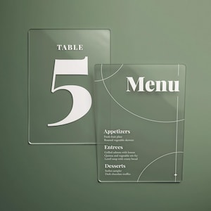 Puede incluir: Dos letreros de acrílico transparente sobre un fondo verde. Uno muestra "TABLE 5" en blanco, el otro lee "Menú" con categorías de alimentos. El diseño es minimalista y moderno, adecuado para restaurantes o eventos. Medidas en cm.