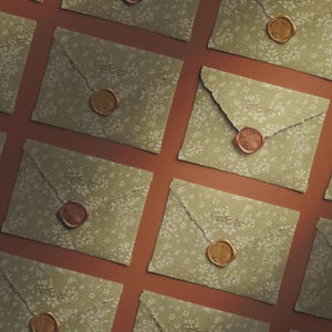 May include: Overhead shot of several sage green envelopes with a floral pattern. Each envelope is sealed with a wax stamp in either a copper or gold color. One envelope is partially open, revealing the interior.