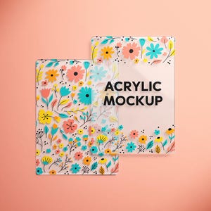 May include: Two clear acrylic mockups with floral designs in shades of pink, yellow, and blue. The text "ACRYLIC MOCKUP" is displayed in black. The background is a solid peach color.
