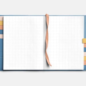 May include: A blue leather-bound journal with a gridded page, a pink ribbon bookmark, and colorful sticky notes. The journal has a pen holder and a pen.