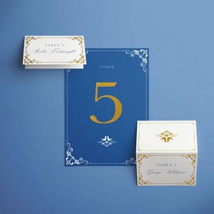 Puede incluir: Una tarjeta azul con el número de mesa 5 en dorado y dos tarjetas de sitio. Las tarjetas de sitio y la tarjeta con el número de mesa tienen bordes y texto decorativos dorados. El fondo es azul liso.