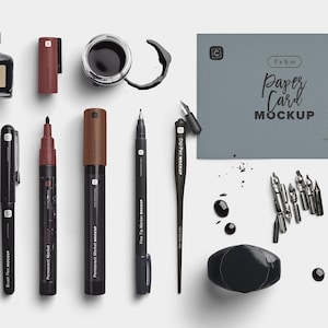 Puede incluir: Una vista cenital de artículos de papelería, que incluyen una botella de tinta negra, bolígrafos, rotuladores y una regla. También hay una maqueta de tarjeta de papel gris con el texto "Paper Card Mockup". Salpicaduras de tinta y plumillas están dispersas.
