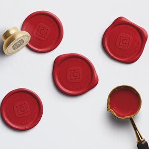 May include: An assortment of red wax seals and a gold-toned wax stamp and melting spoon. The seals have a circular design with a letter "C" in the center. The wax melting spoon has a black handle.