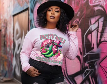 May include: A light pink long-sleeve shirt with the text "PRETTY GIRLS" and a graphic of cowboy boots, a hat, and flowers. The shirt is paired with black jeans and a black hat.