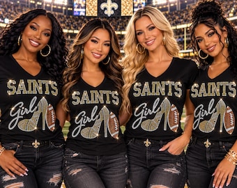 May include: Four black V-neck t-shirts featuring a rhinestone graphic that reads SAINTS in block letters above the word girl in script. The design includes a high-heeled shoe and a football, both embellished with gold and brown rhinestones.