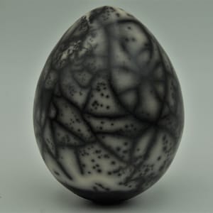 Peut inclure: Un œuf en céramique avec un glaçage craquelé noir et blanc. L'œuf a une surface rugueuse et texturée.