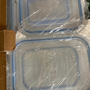 以下が含まれることがあります： 透明な長方形の食品保存容器で、蓋に青いアクセントが付いています。容器は透明なプラスチックで包まれ、段ボール箱の中に積み重ねられています。