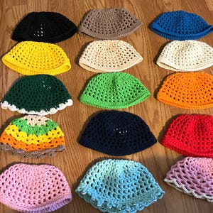 May include: A collection of 15 crocheted hats in various colors, including pink, blue, green, yellow, orange, red, and brown. The hats are all made with a similar stitch pattern and have a rounded shape.
