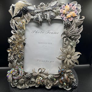 May include: Ornate silver-toned photo frame with floral and butterfly embellishments. The frame has a rectangular opening with the text "Photo Frame" and "A heart for you". Service size is 3" x 5".