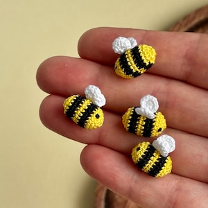 May include: Four small, handcrafted crochet bees featuring yellow and black striped bodies with tiny white wings. Each bee is constructed with a textured yarn finish, showcasing a rounded shape and detailed stitching throughout the insect design.