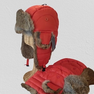 May include: Two red quilted winter hats with faux fur ear flaps. The hats have a puffy, quilted design and are made of a soft, warm material.