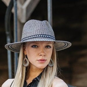 May include: A woman wearing a gray and black fedora with a black and white patterned band. The hat has a wide brim and is made of a woven material.