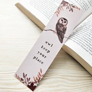 Puede incluir: Un marcap&aacute;ginas rosa y marr&oacute;n con una ilustraci&oacute;n de acuarela de un b&uacute;ho posado en una rama. El marcap&aacute;ginas tiene el texto "owl keep your place" impreso en &eacute;l.