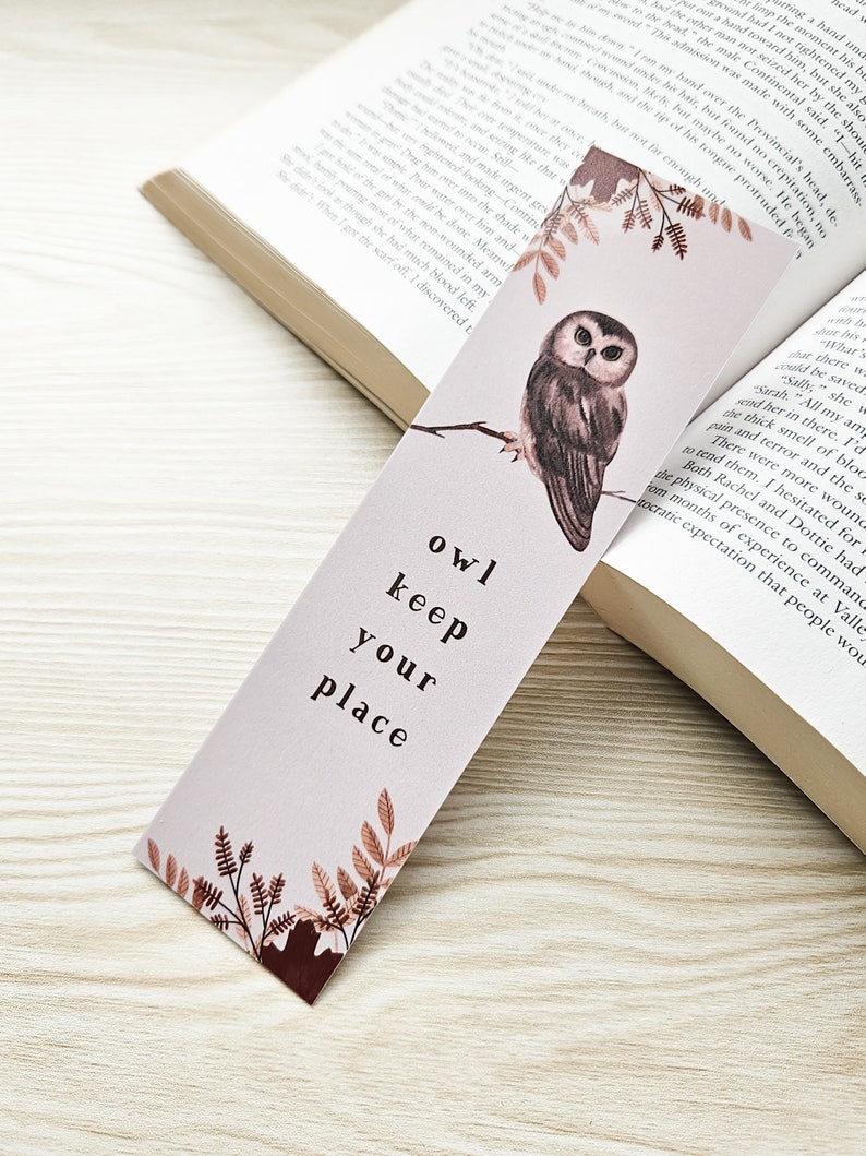 Puede incluir: Un marcap&aacute;ginas rosa y marr&oacute;n con una ilustraci&oacute;n de acuarela de un b&uacute;ho posado en una rama. El marcap&aacute;ginas tiene el texto "owl keep your place" impreso en &eacute;l.