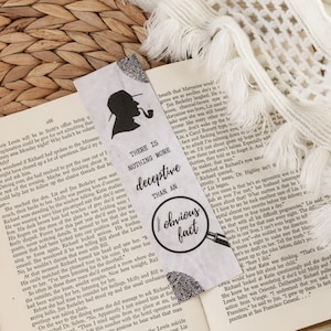 May include: A white bookmark featuring a black silhouette of a detective holding a pipe. The bookmark includes the text "There is nothing more deceptive than an obvious fact" and a magnifying glass with a fingerprint.