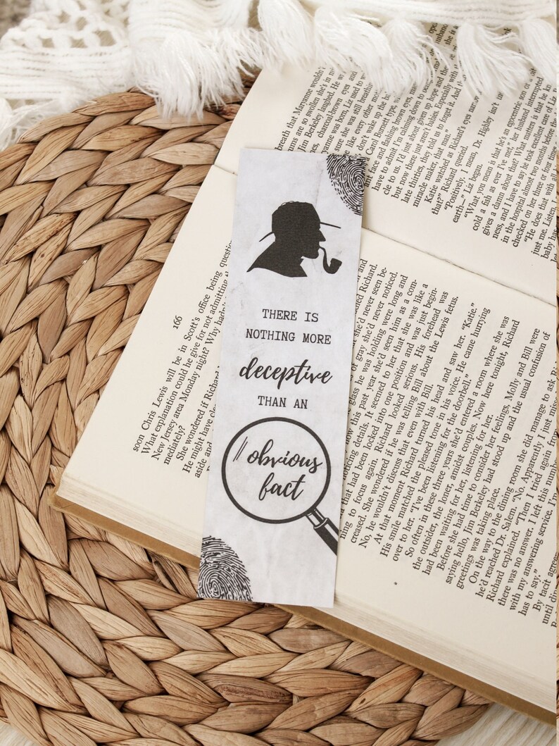 May include: A white bookmark featuring a black silhouette of a person wearing a hat and smoking a pipe. The bookmark has the text "There is nothing more deceptive than an obvious fact."