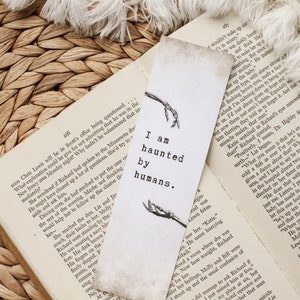 Puede incluir: Un marcap&aacute;ginas blanco con un dise&ntilde;o de esqueleto negro y el texto "Estoy obsesionado por los humanos". El marcap&aacute;ginas est&aacute; sobre un libro con p&aacute;ginas marrones.