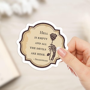 May include: A sticker featuring a quote from Shakespeare: "Hell is empty and all the devils are here." The design includes a rose held by a skeleton hand. The sticker has a tan background with a dark brown border.