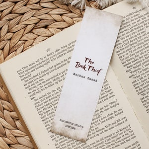 Puede incluir: Un marcap&aacute;ginas marr&oacute;n y blanco con el t&iacute;tulo "El ladr&oacute;n de libros" de Markus Zusak. El marcap&aacute;ginas est&aacute; hecho de papel y tiene un aspecto vintage.
