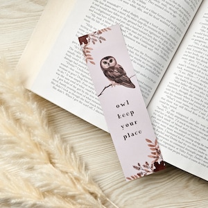 Puede incluir: Un marcap&aacute;ginas rosa con una ilustraci&oacute;n de b&uacute;ho marr&oacute;n y el texto "owl keep your place". El marcap&aacute;ginas tiene un dise&ntilde;o floral con hojas marrones y rosas.