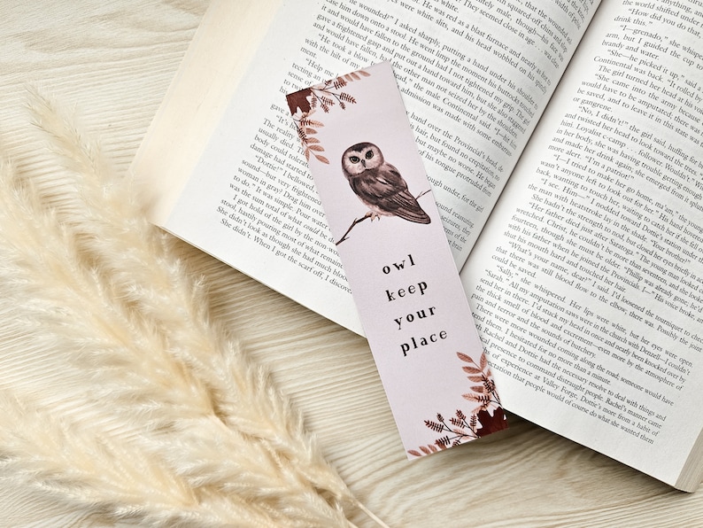 Puede incluir: Un marcap&aacute;ginas rosa con una ilustraci&oacute;n de b&uacute;ho marr&oacute;n y el texto "owl keep your place". El marcap&aacute;ginas tiene un dise&ntilde;o floral con hojas marrones y rosas.