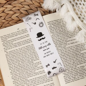 Puede incluir: Marcap&aacute;ginas de dise&ntilde;o vintage con sombrero, bigote, pipa y otros iconos de caballero. El marcap&aacute;ginas tiene el texto "IT IS THE little grey cells men ami ON WHICH ONE MUST RELY" y est&aacute; colocado en un libro abierto.