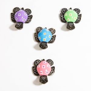 May include: Four hand-painted wooden turtle figurines with floral designs. The turtles are painted in shades of purple, green, blue, and pink with white flowers.